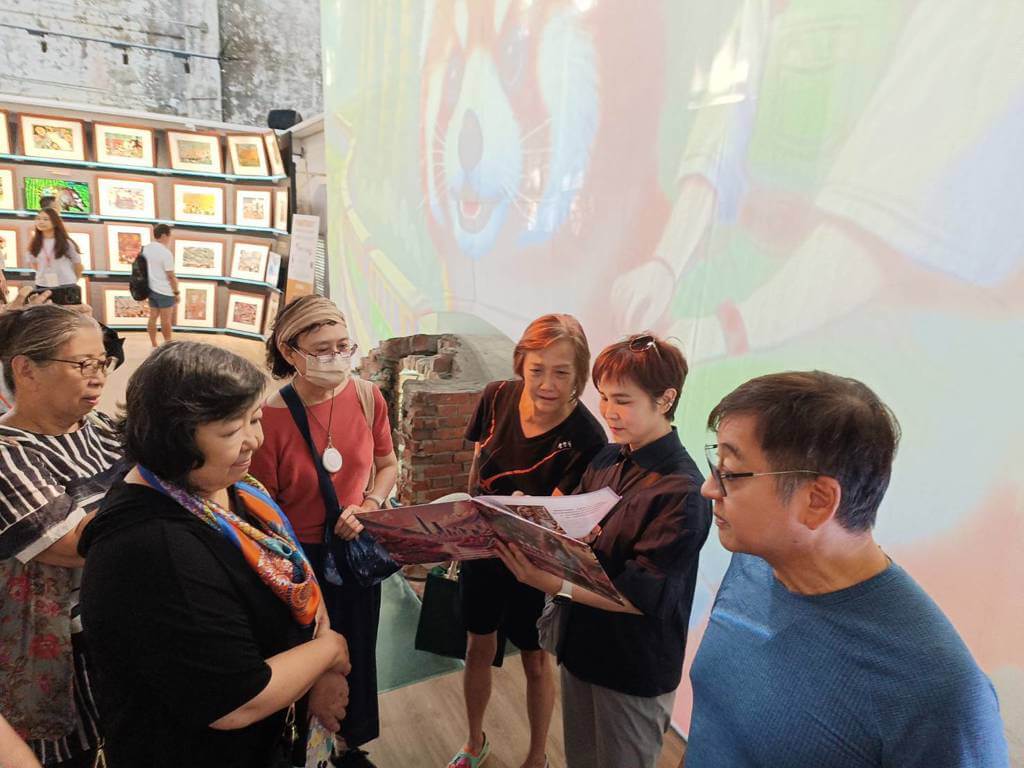 李艷秋在現場，為前來捧場的<女記者作家協會>好友們熱心導覽，以實際行動支持夫婿李濤的理想。圖／刁明芳